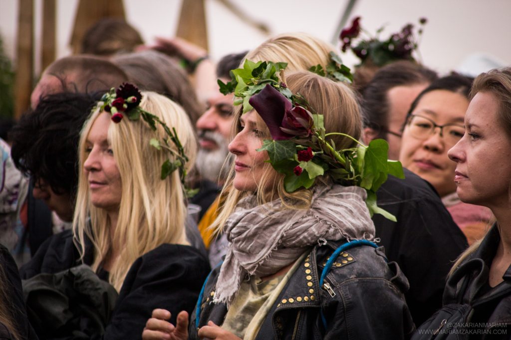 To lyshårede kvinder står med blomsterkranse i håret og kigger